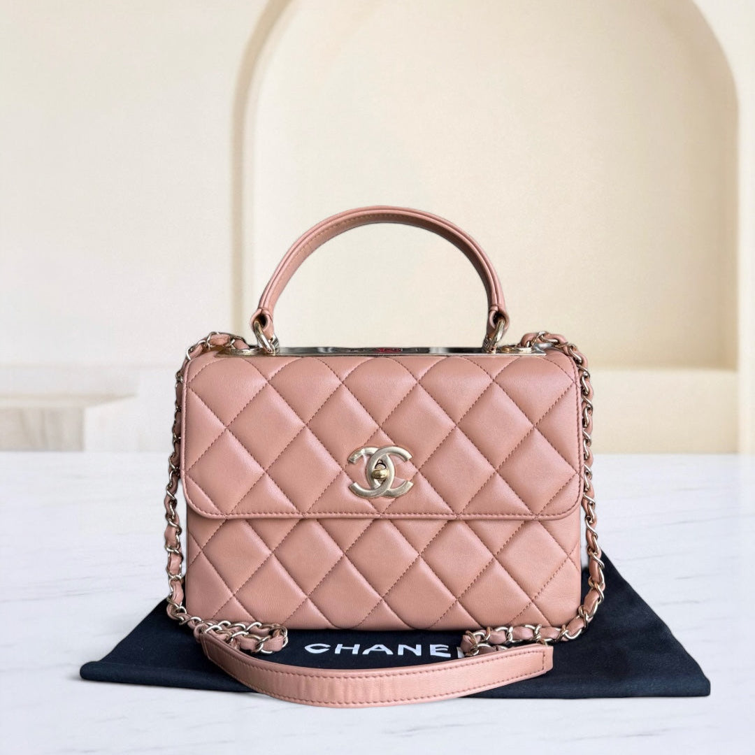 Pink quilted handbag with gold chain and handle on a black mat with 'Chanel' branding.