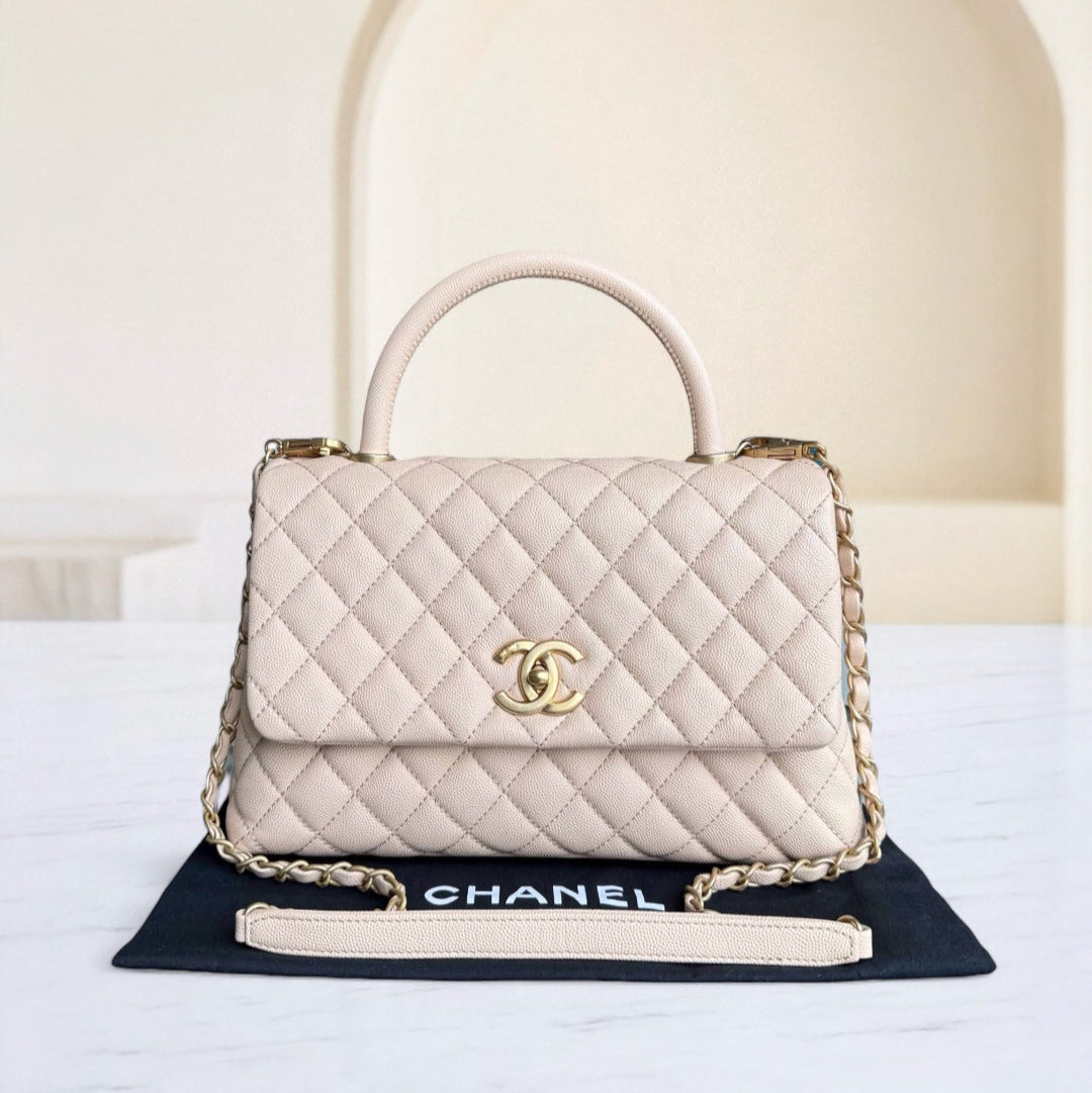 Quilted beige handbag with gold chain on a white surface with a blurred background