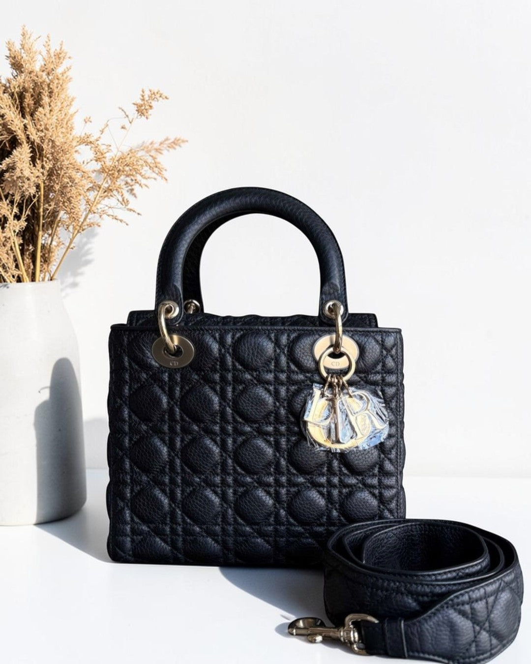Black quilted handbag with gold hardware and a clear crystal charm on a white surface.