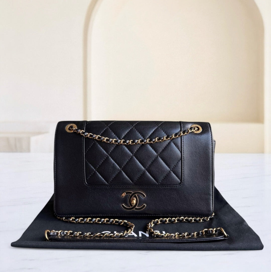 Black quilted handbag with gold chain and clasp on a white surface.