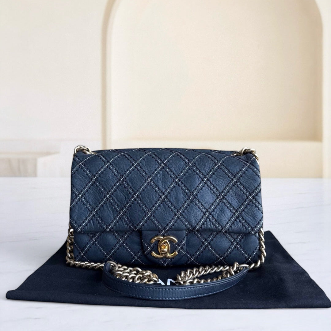 Blue quilted handbag with gold chain on a white surface