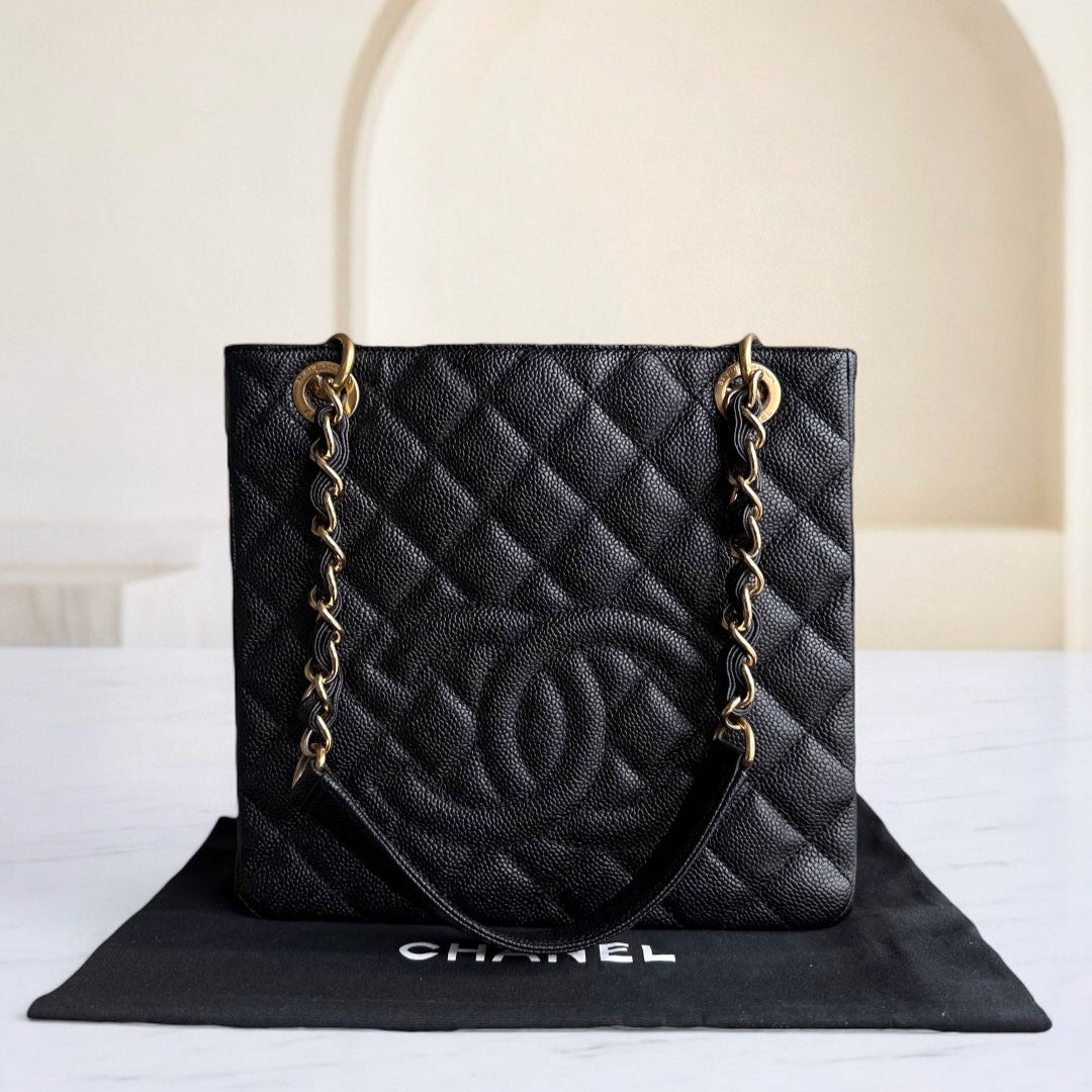 Black quilted handbag with gold chain on a white surface with a beige background