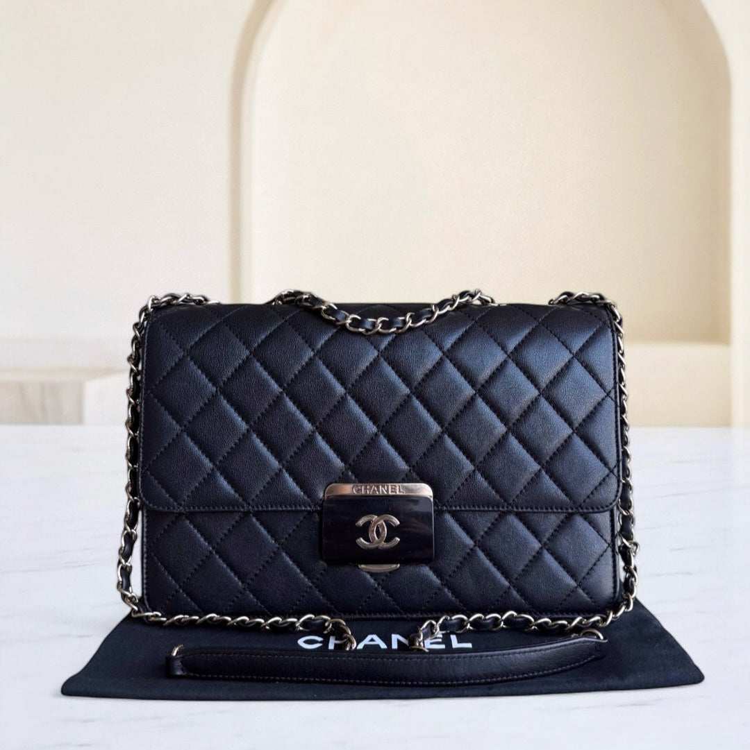 Black quilted Chanel handbag with chain strap on a white surface.