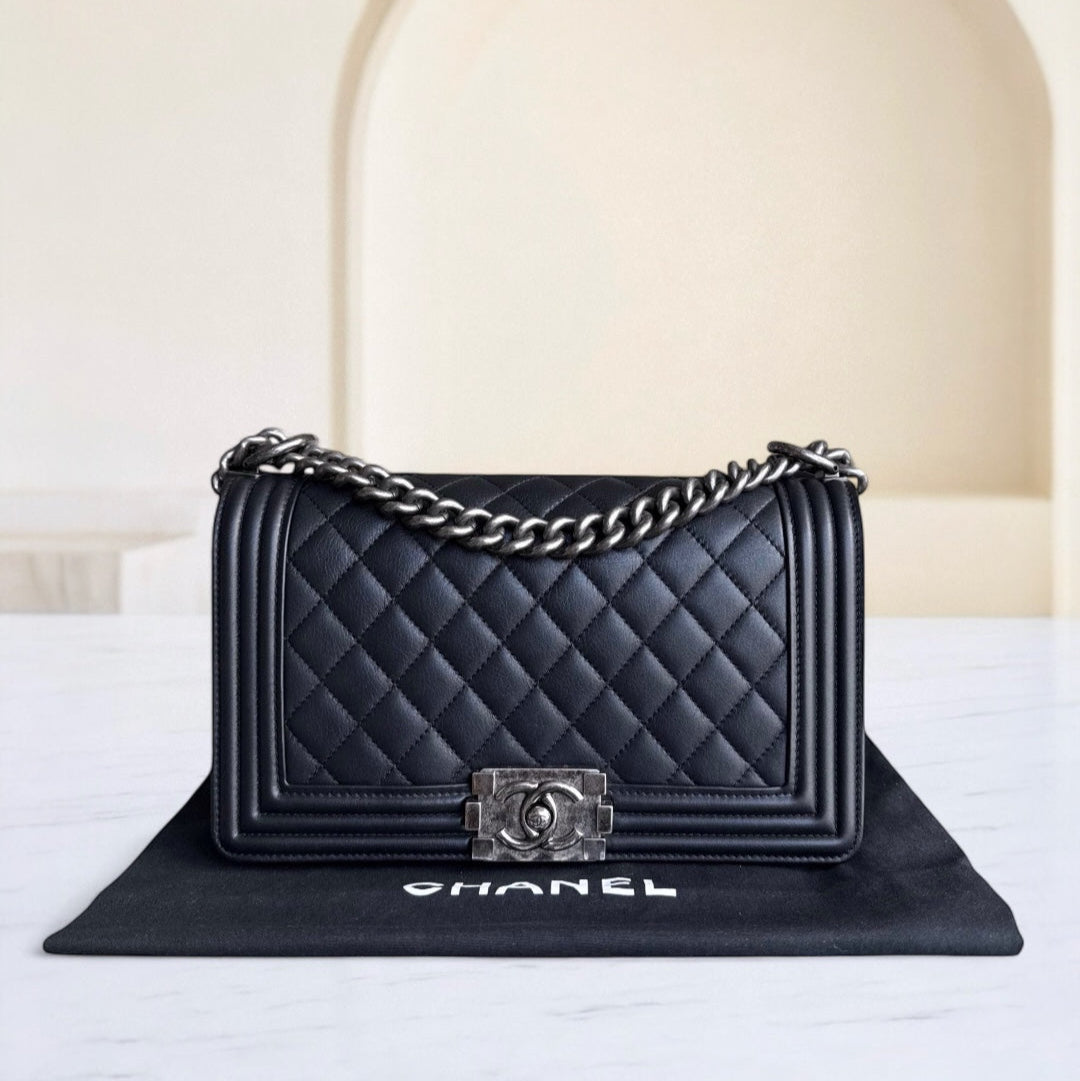 Black quilted Chanel handbag with silver chain on a white surface.