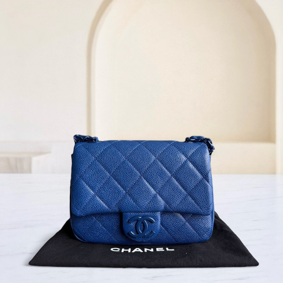 Blue quilted Chanel handbag on a black mat with a white background