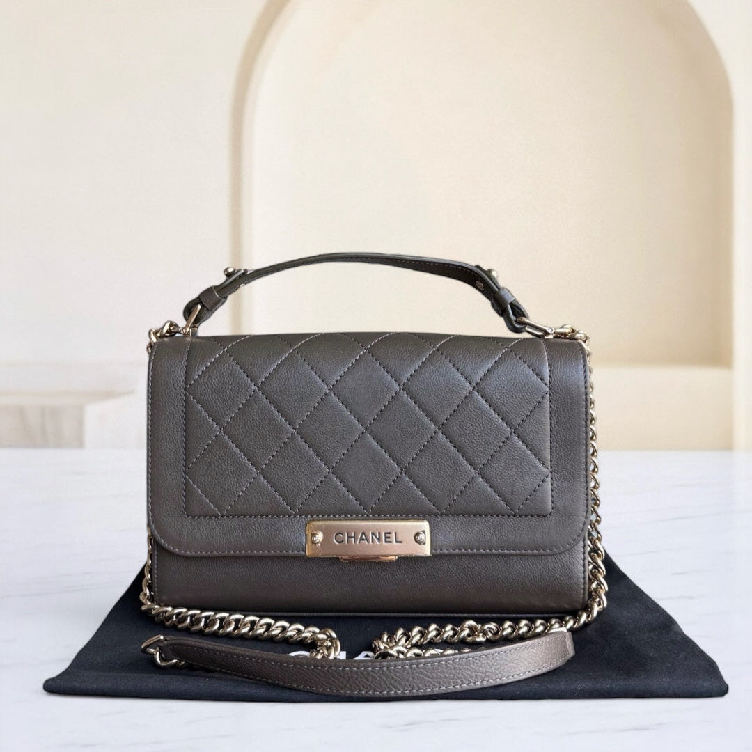 Gray quilted handbag with gold chain detail on a white surface