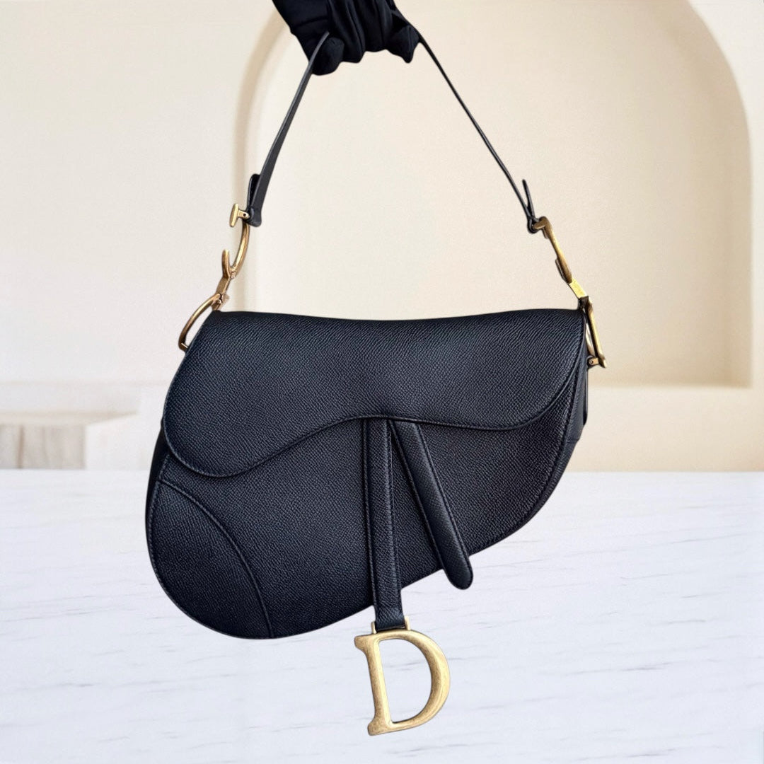 Black handbag with gold accents held by a gloved hand against a neutral background