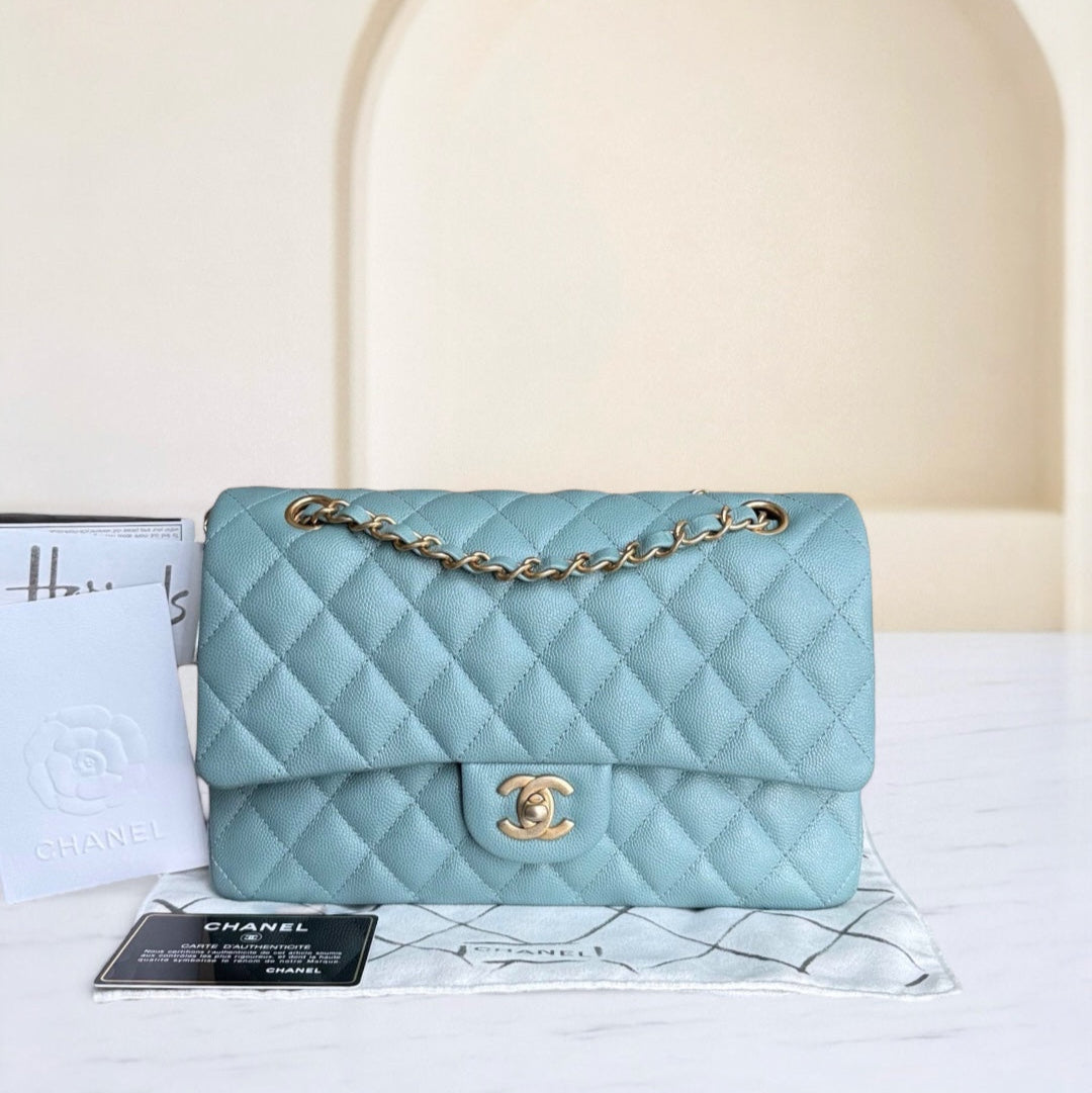 Light blue quilted handbag with gold chain on a white surface with a beige arch in the background