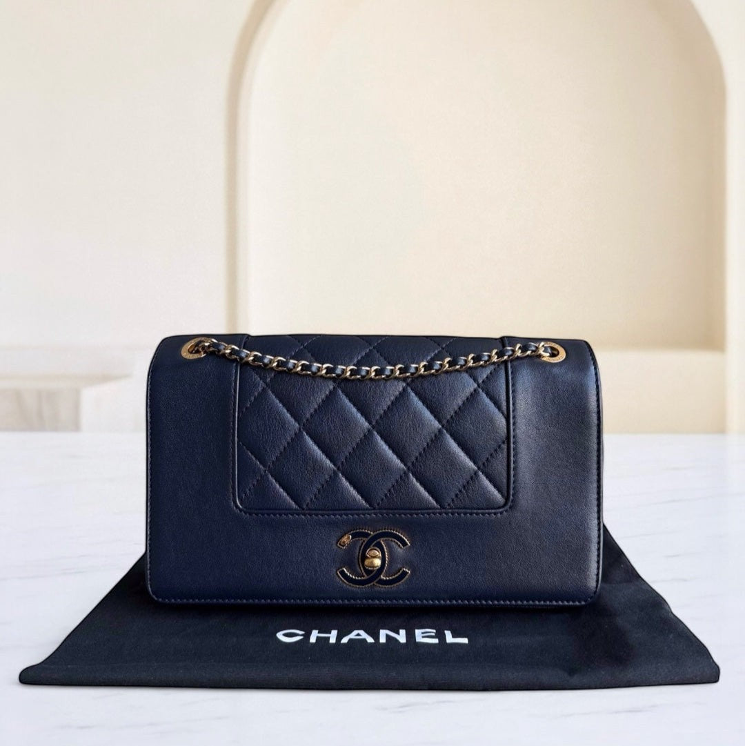 Navy blue quilted Chanel handbag on a black Chanel mat with a white background