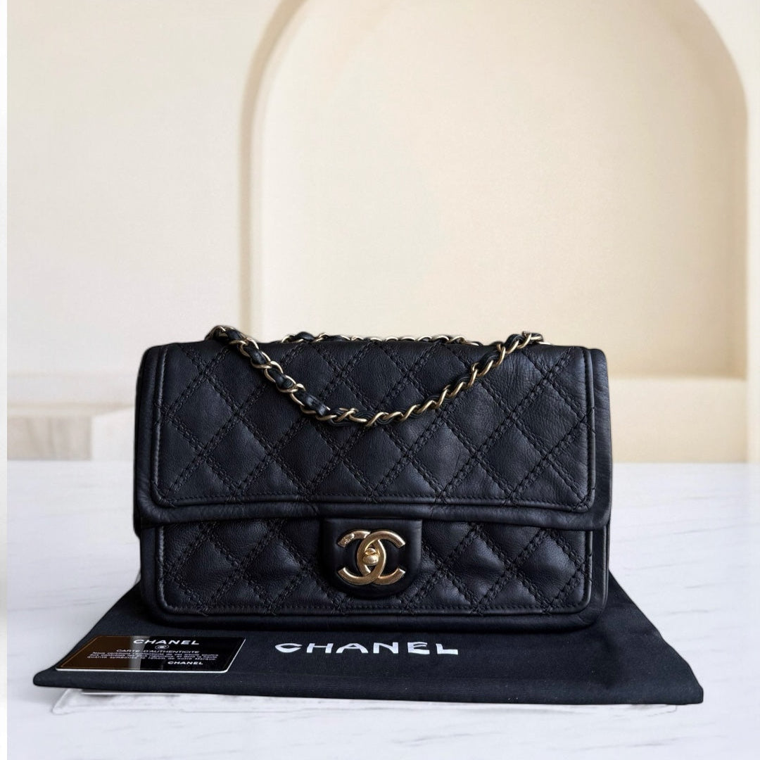 Black quilted Chanel handbag with gold chain on a white surface