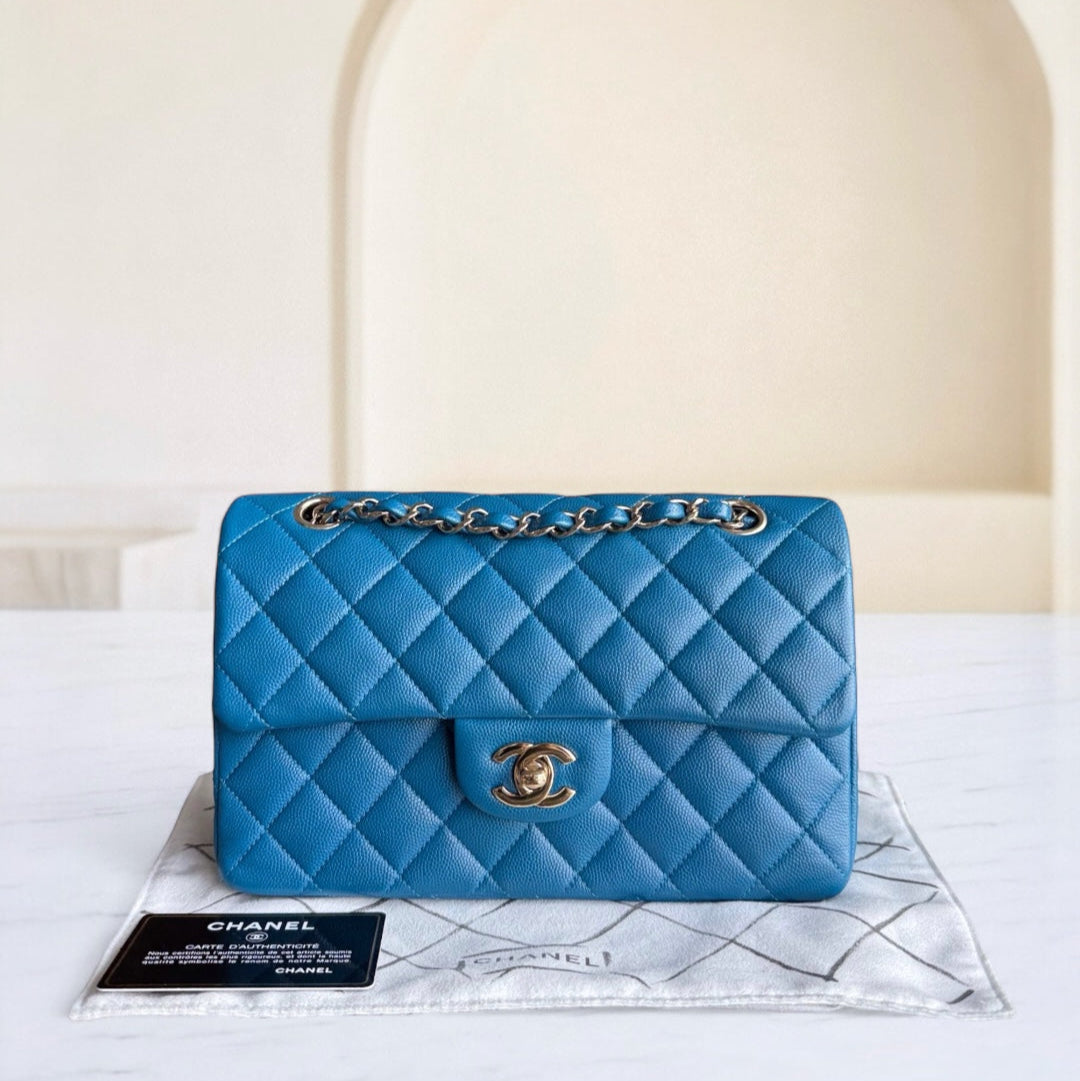 Blue quilted handbag with gold chain on a white surface with a beige background