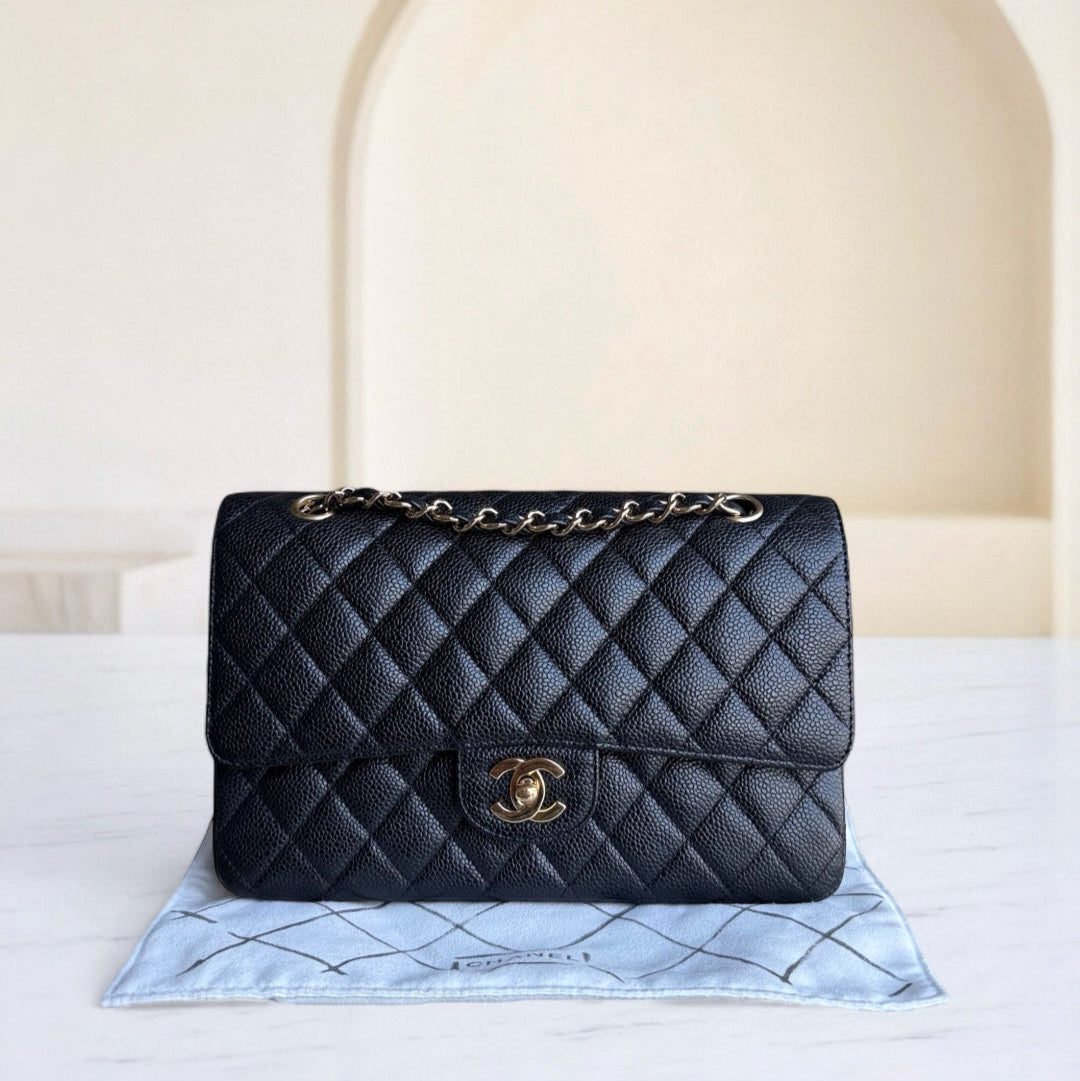 Black quilted handbag with gold chain on a light blue mat