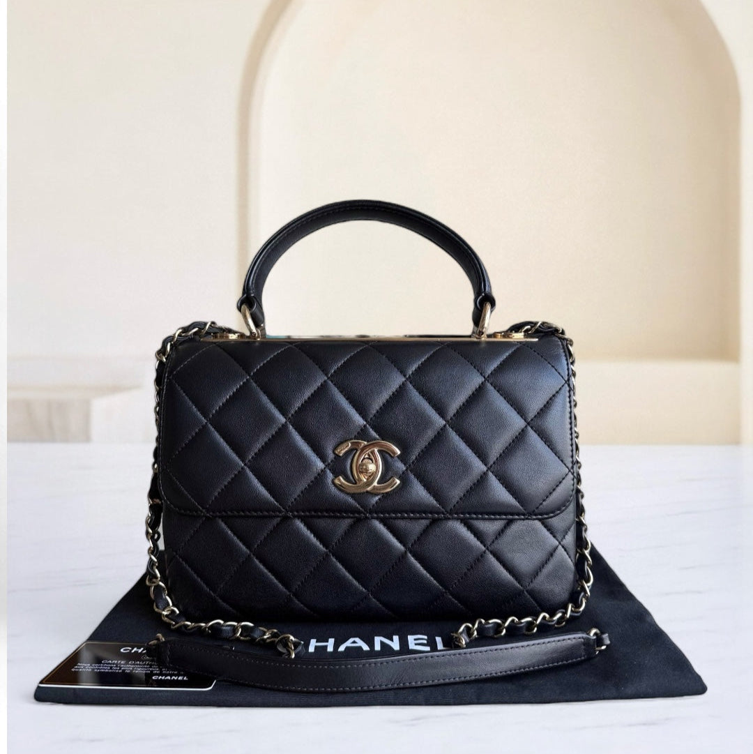 Black quilted handbag with gold chain and logo on a white surface