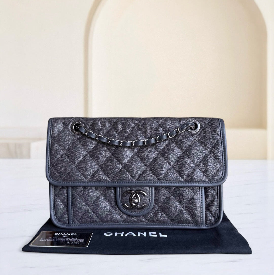 Gray quilted Chanel handbag on a white surface with a neutral background