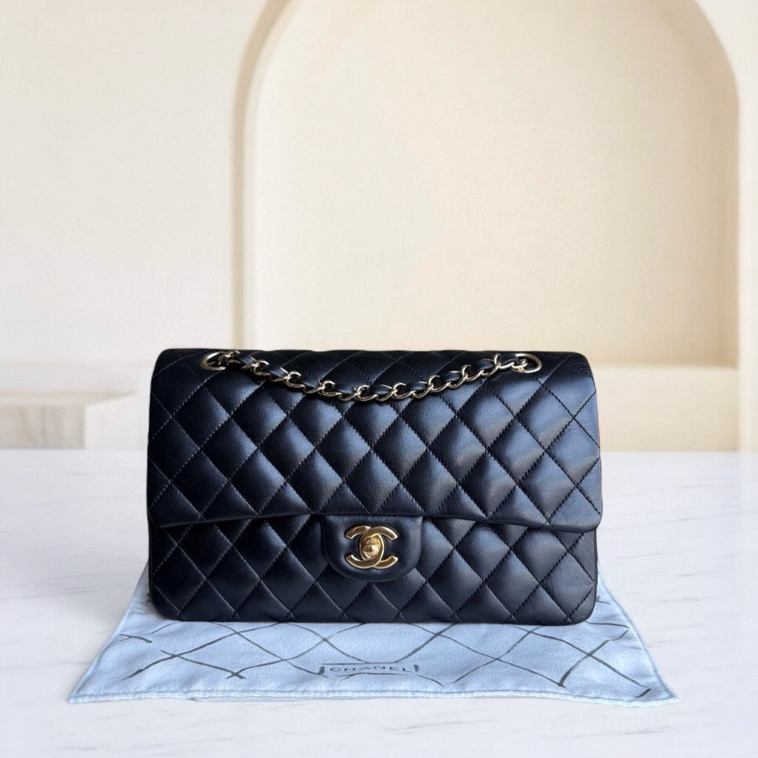 Black quilted handbag with gold chain on a light blue cushion