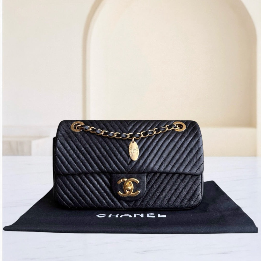 Black quilted Chanel handbag with gold chain on a white surface with a beige background