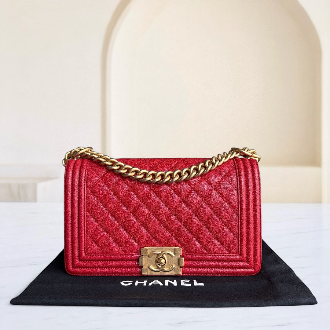Red Chanel handbag with gold chain and clasp on a black mat with 'Chanel' branding.