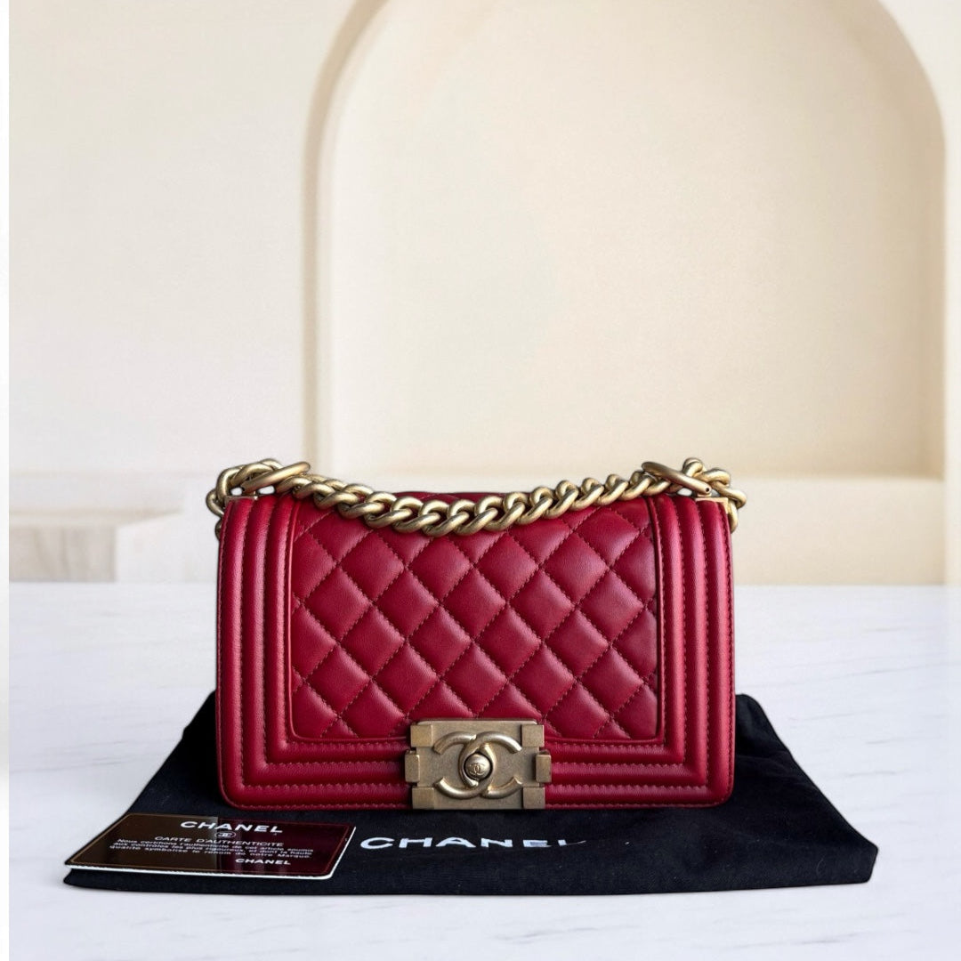 Red quilted handbag with gold chain and clasp on a black Chanel dust bag.